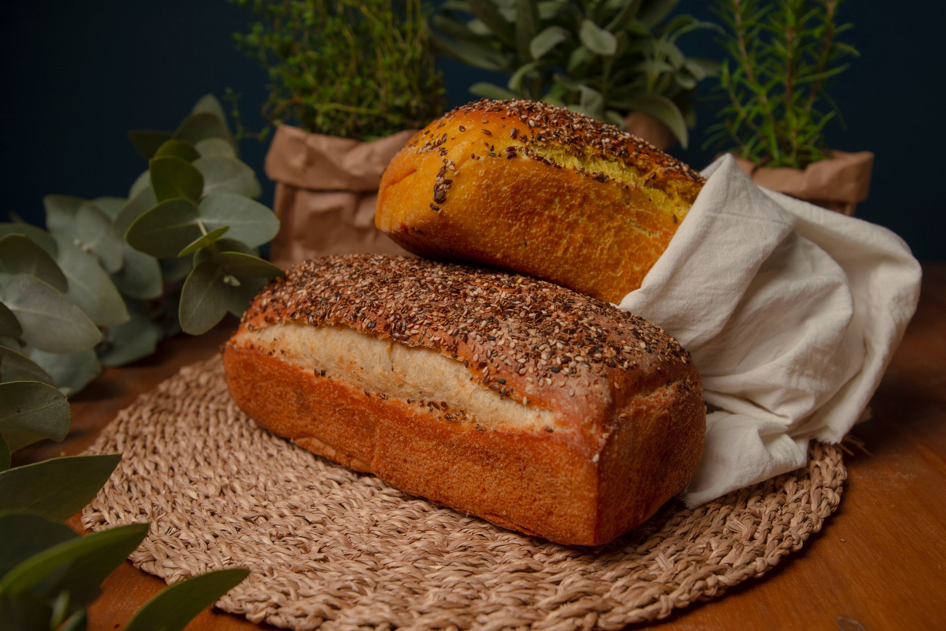 Two artisan loaves of bread surrounded by fresh herbs create a rustic kitchen setting.