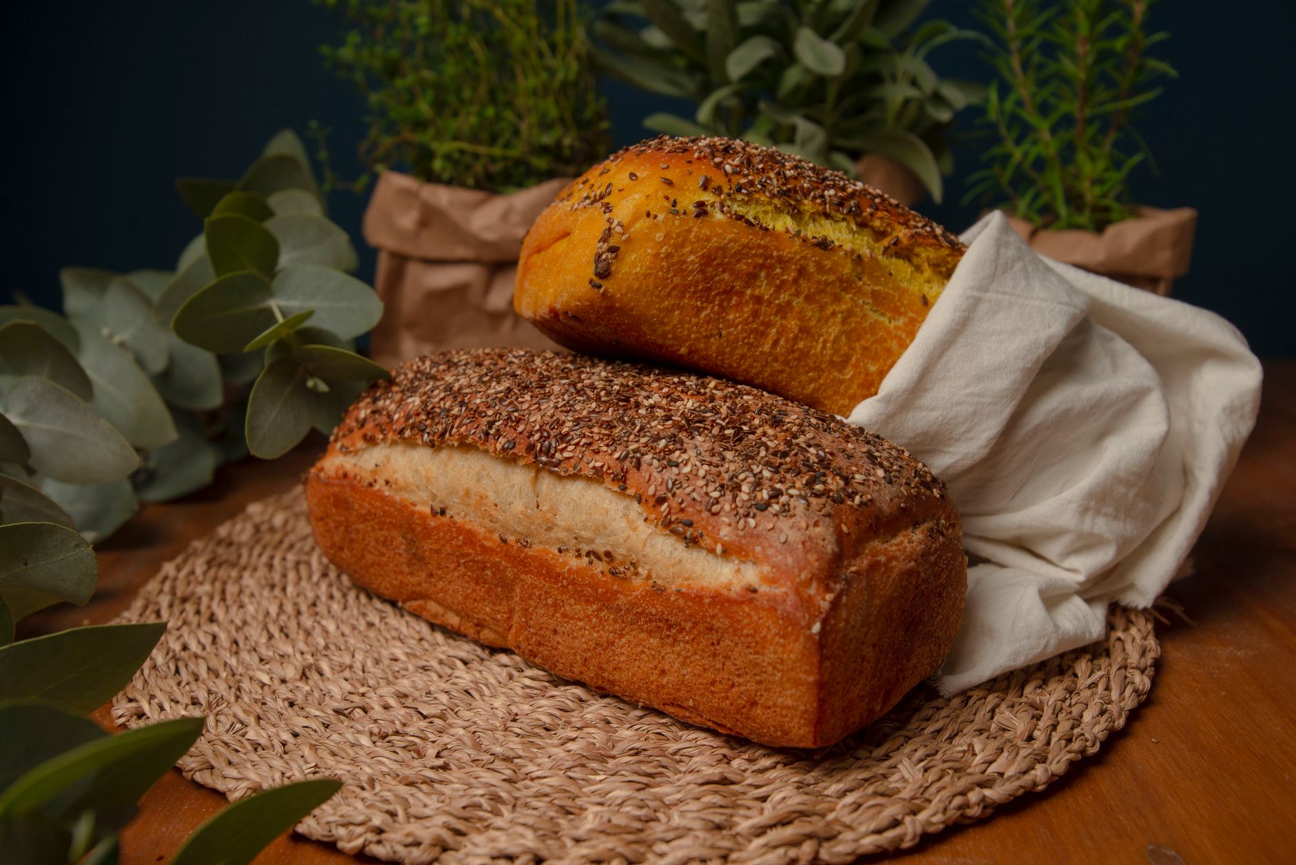 Two artisan loaves of bread surrounded by fresh herbs create a rustic kitchen setting.