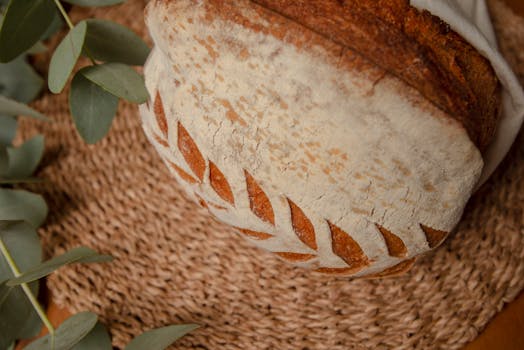 Close-up of crusty artisan bread with decorative scoring on woven placemat.