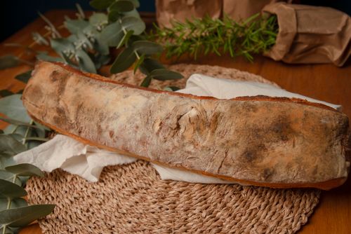 Free A crusty artisan baguette displayed on a woven mat with greenery, creating a rustic ambiance. Stock Photo