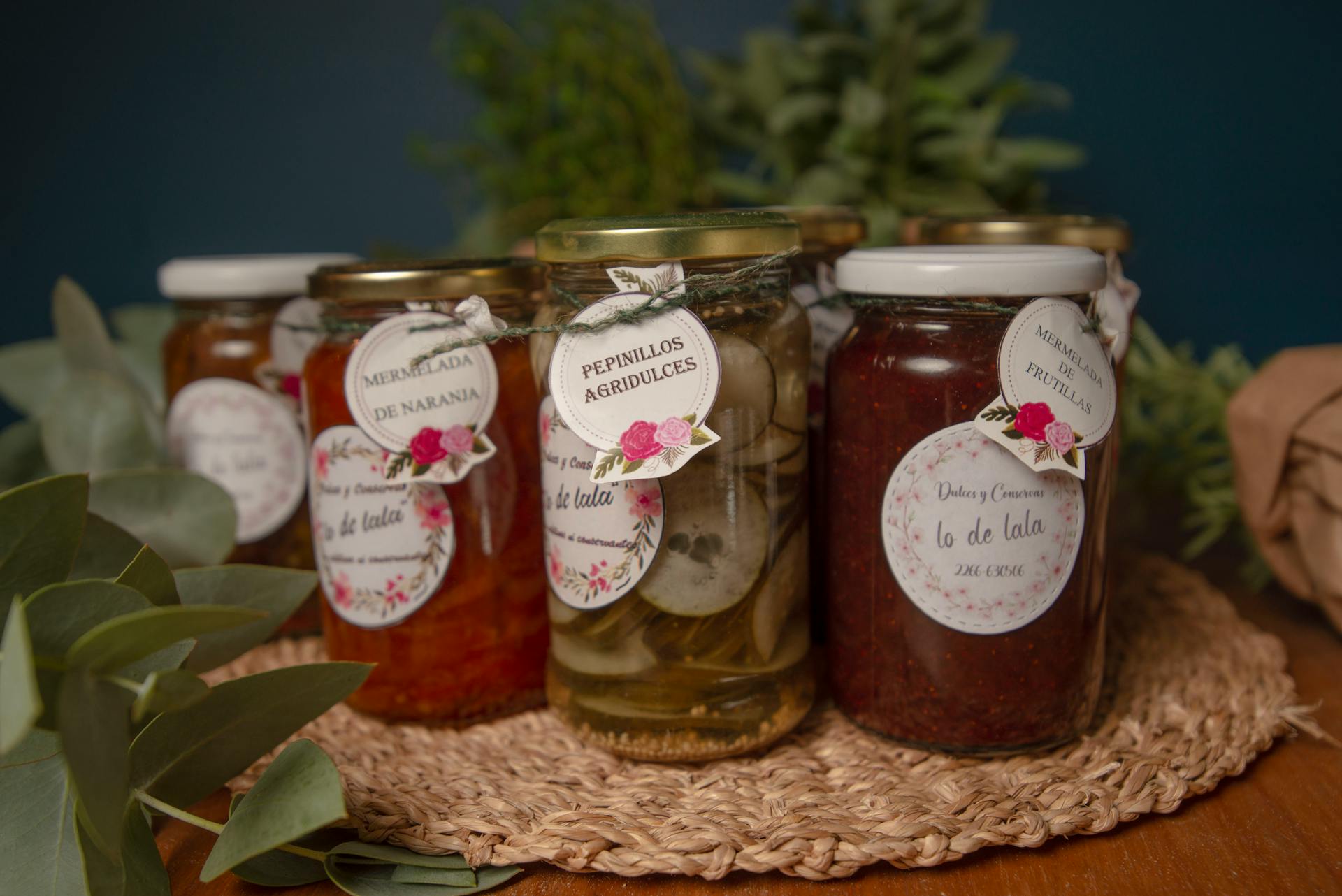 A collection of artisanal homemade jams and pickles in glass jars with floral labels.