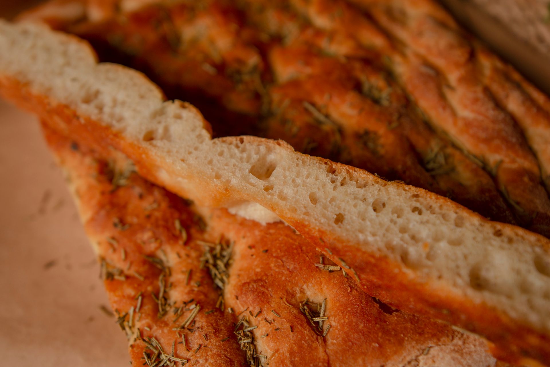 Freshly baked focaccia bread topped with rosemary herbs, showcasing a golden crust and airy texture.