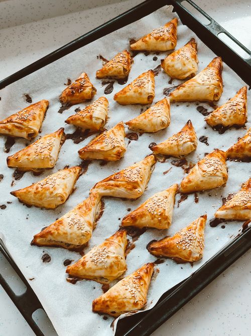 Free Close-up of freshly baked golden triangular pastries on a tray with sesame seeds. Stock Photo