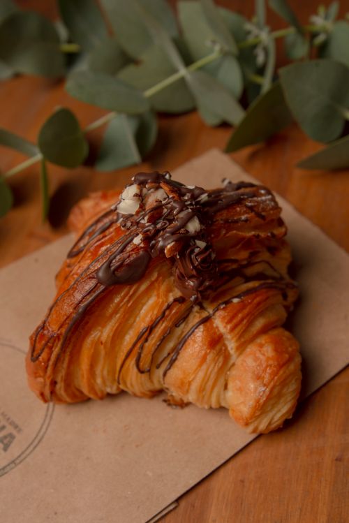 Free A rich croissant with chocolate drizzle and nuts on a wooden table. Stock Photo
