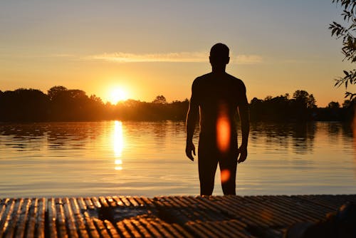 Silhouette Photo of Man Standing Near Lake