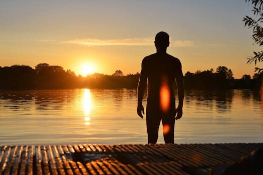 一名男子的剪影，在宁静的湖边，立于壮丽的日落之中