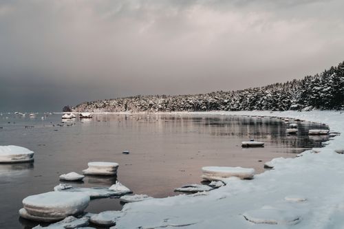 Free Serene view of a snow-covered coast with icy water under a moody winter sky. Stock Photo