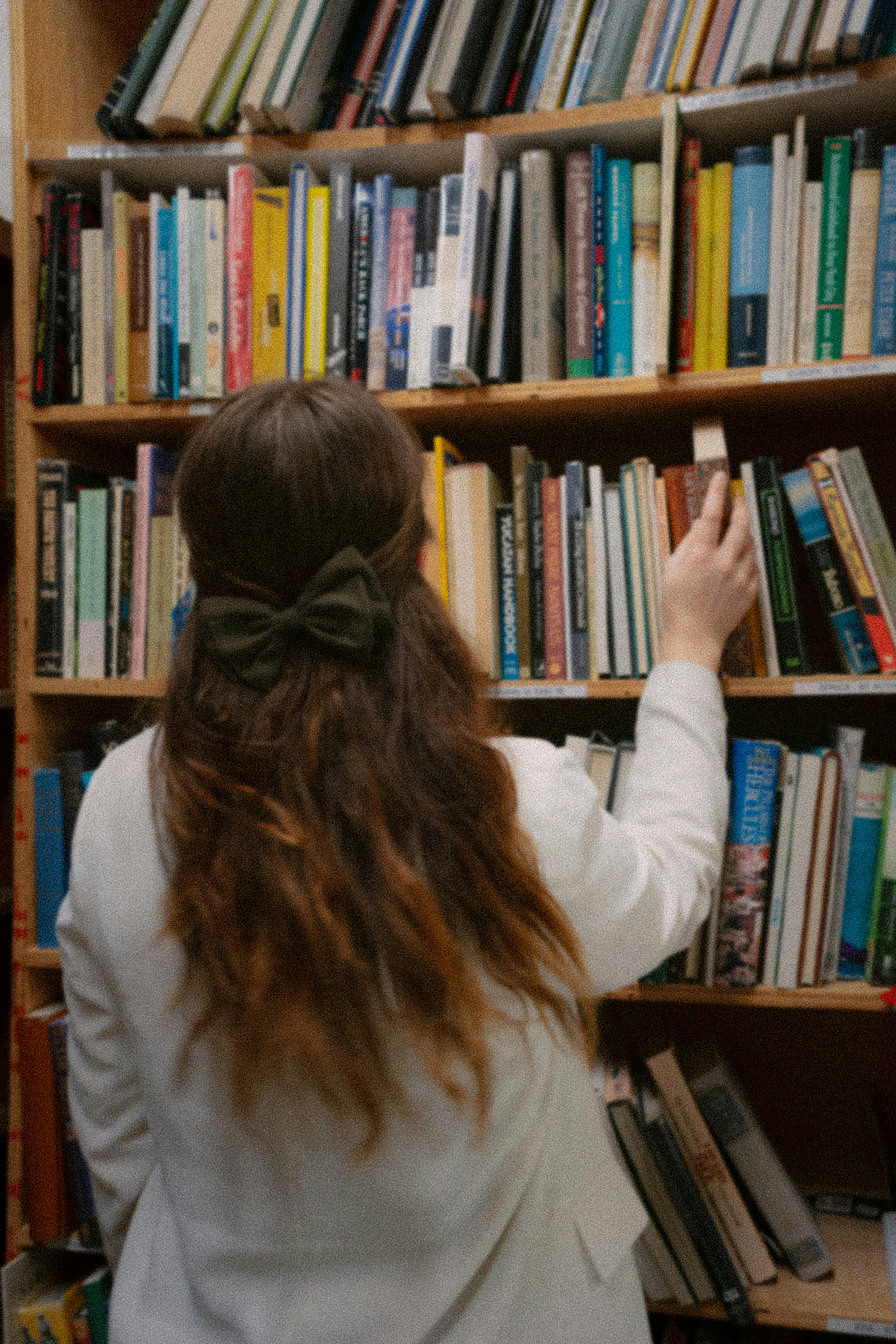 A woman with long hair and a bow selecting a book from a library shelf, portraying a calm reading atmosphere.