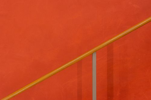 Free A minimalist red wall featuring a simple wooden railing with modern design. Stock Photo