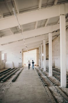 两个人走过一座天花板很高、巨大而空荡荡的工业建筑