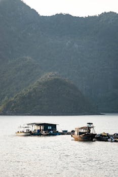 Peaceful scene of fishing boats on a lake surrounded by hills at dusk, creating a serene and tranquil atmosphere.