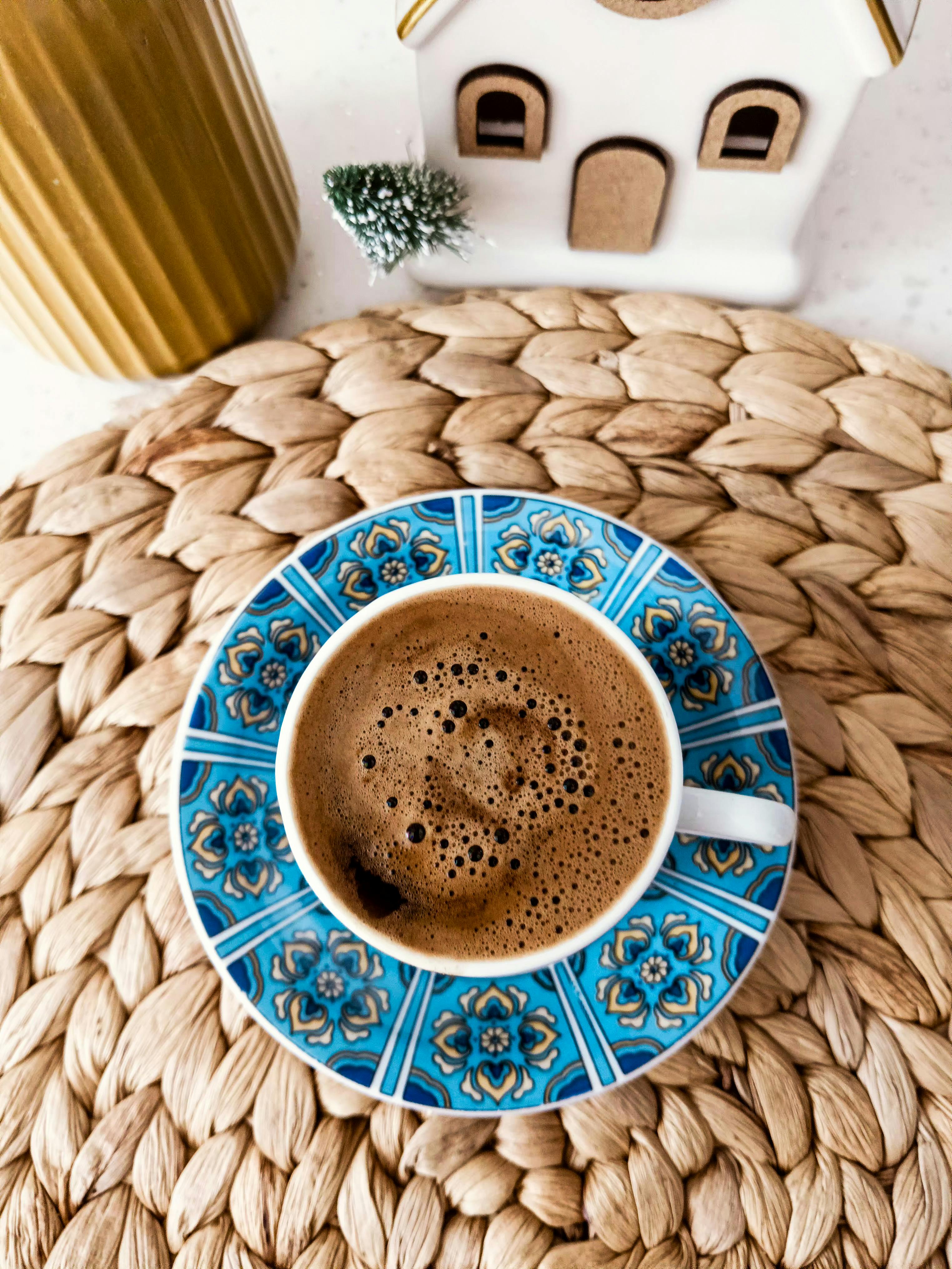 Gratis Taza de café en un platillo azul adornado sobre un mantel tejido con un acogedor fondo de decoración del hogar. Foto de stock