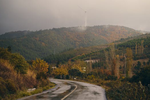 Winding road through autumn hills with a windmill in the distance after rain.