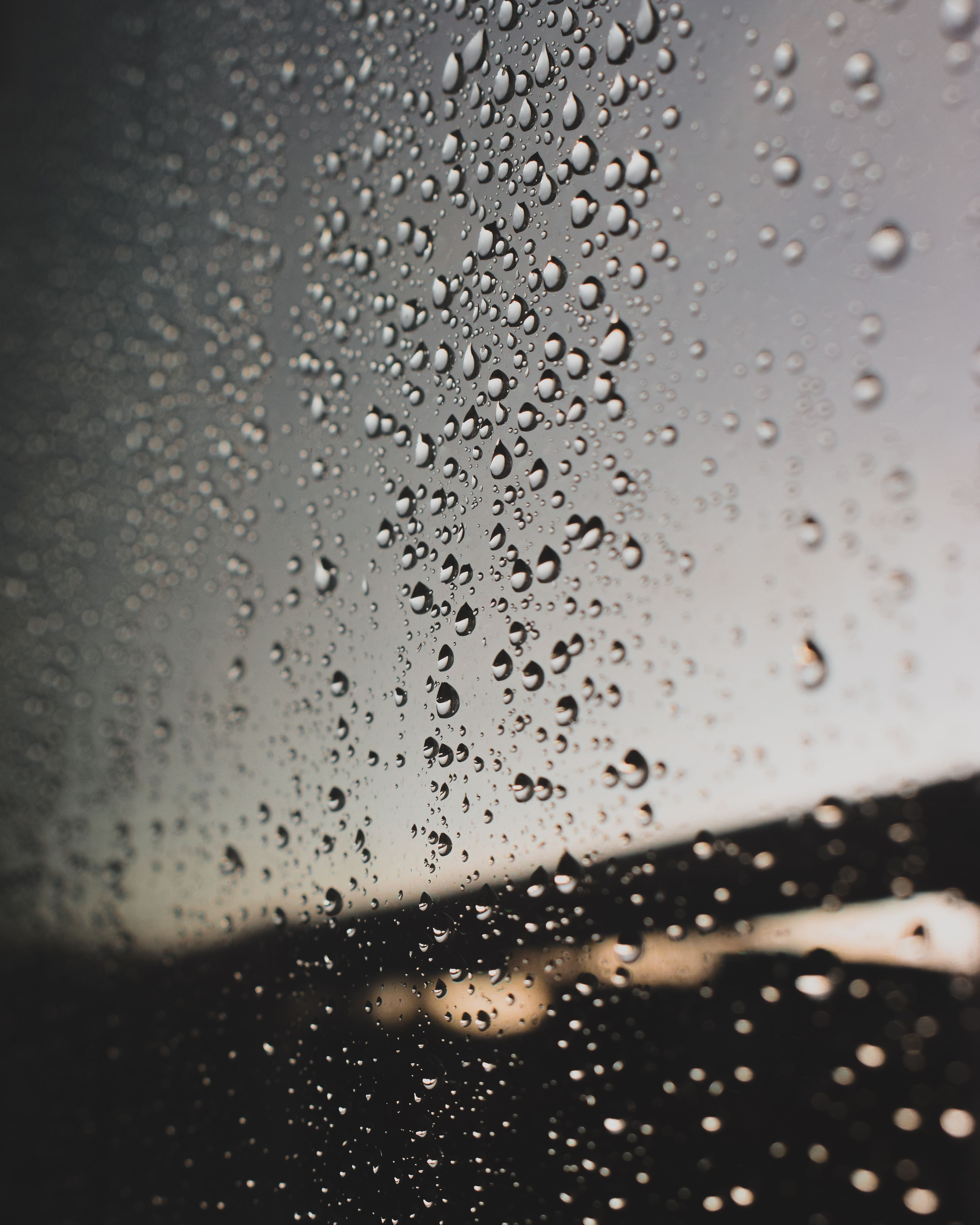 Raindrops on a window with a moody, gloomy evening background, capturing urban rain atmosphere.