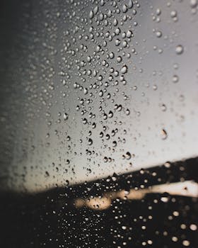 Raindrops on a window with a moody, gloomy evening background, capturing urban rain atmosphere.