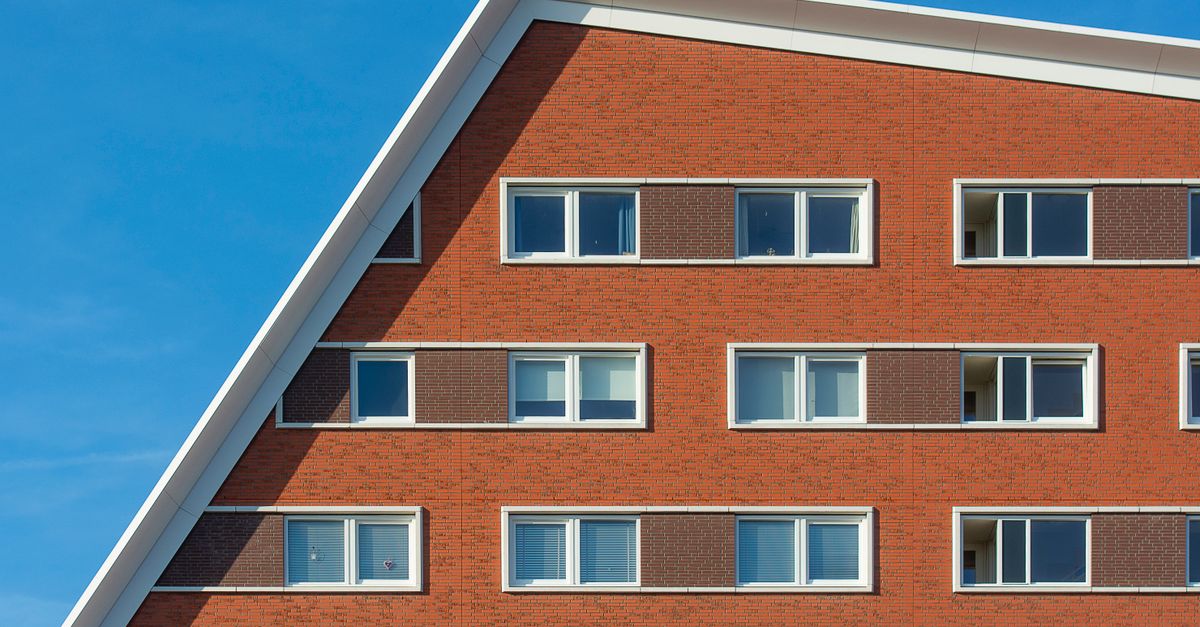 Angular facade of a modern apartment building in Den Haag with vibrant red bricks and windows.