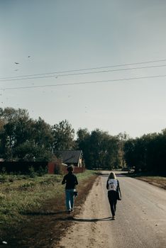 晴朗的天空下，两个人走在绿树成荫的乡村道路上