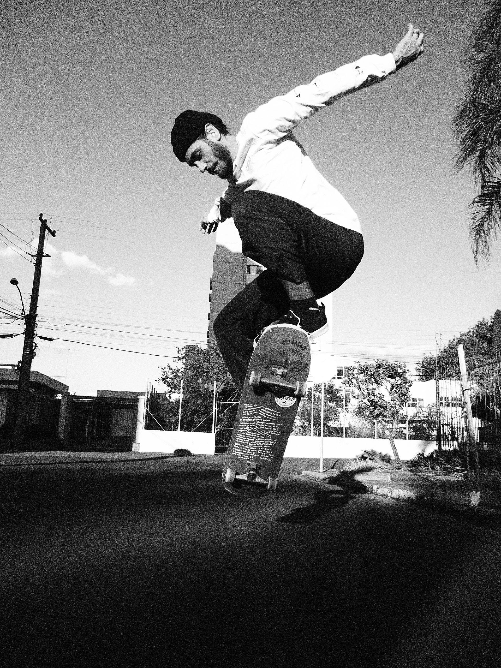 Black and white photo of a skateboarder performing an ollie on a city street.