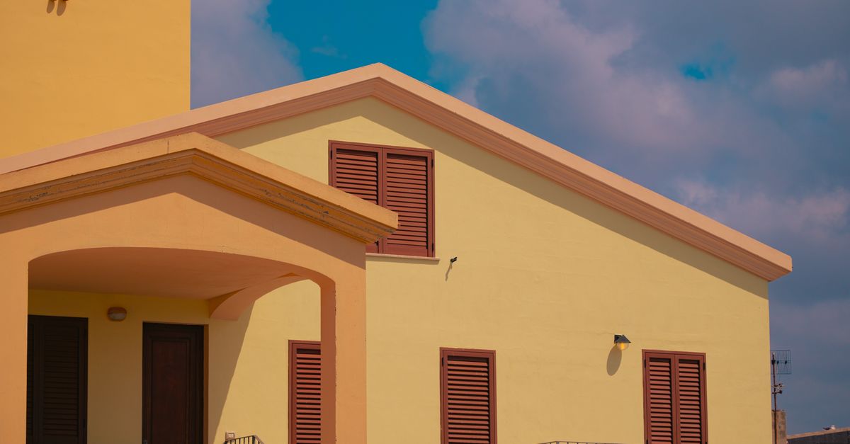 A vibrant yellow house with closed wooden shutters under a blue sky.