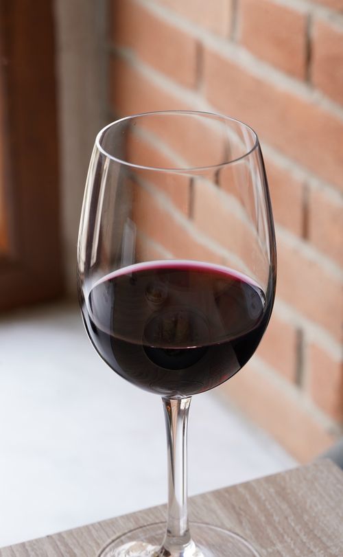 Free A glass of red wine on a wooden table, set against a brick wall backdrop. Stock Photo