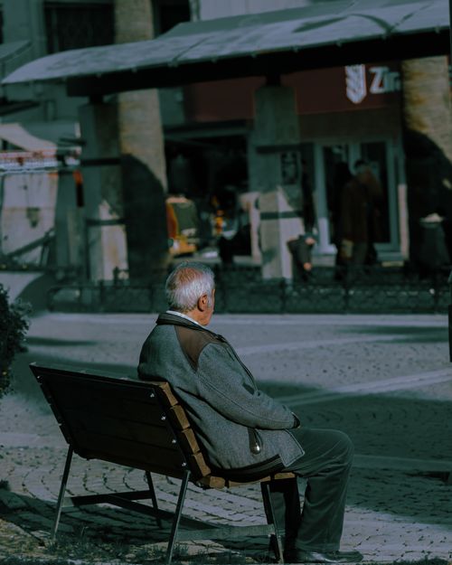 Free Senior man sitting on a park bench in a city square enjoying the day. Stock Photo