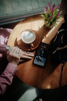 Woman's hand on table with coffee cup and smartphone, cozy café setting.