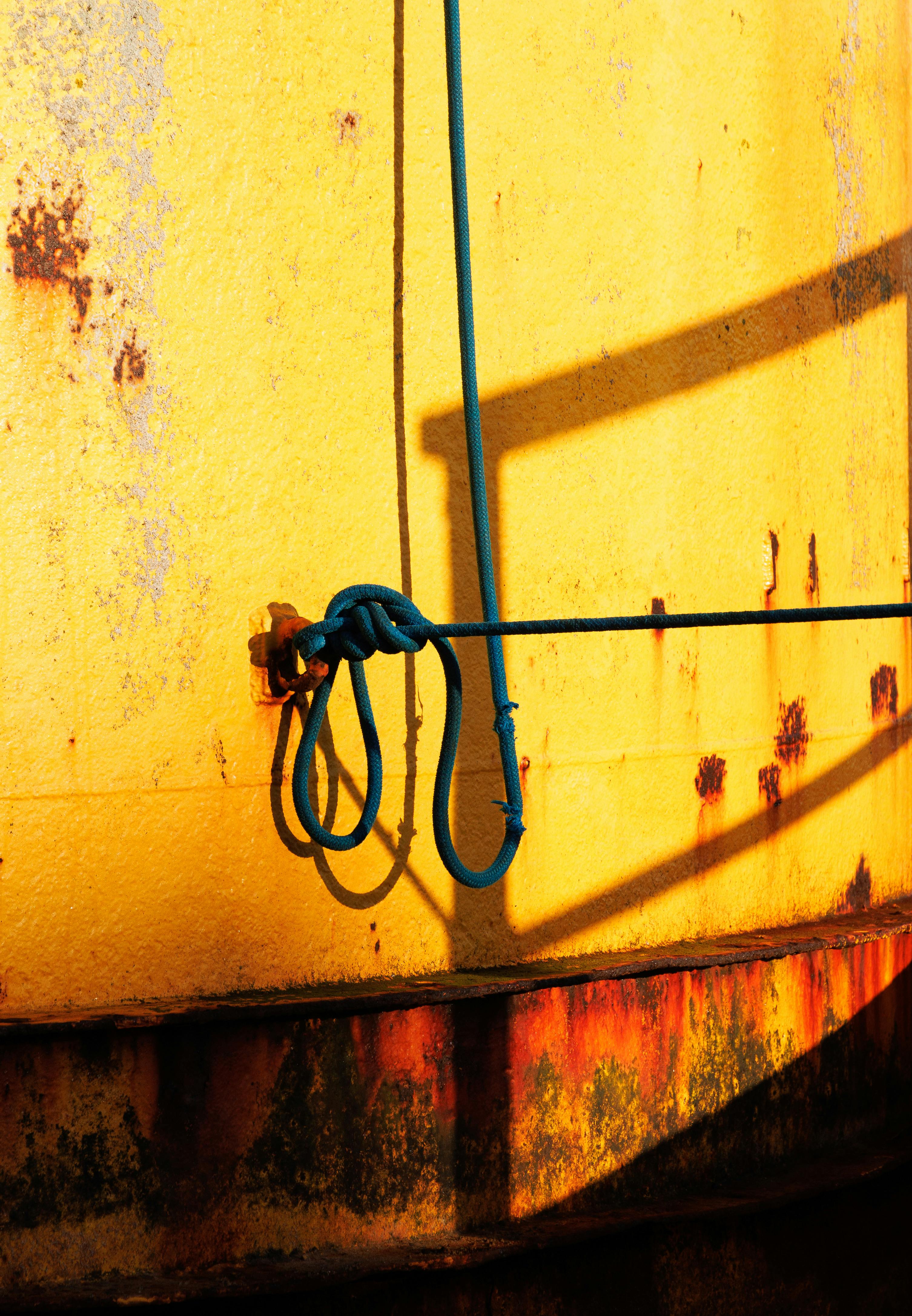 Close-up of blue rope tied on a rust-stained yellow metal surface with shadows.