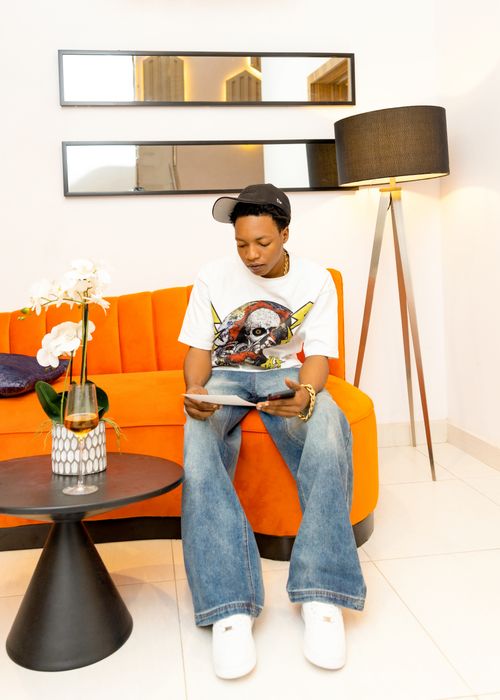 Free A young adult seated on an orange couch reading a tablet in a stylish living room. Stock Photo