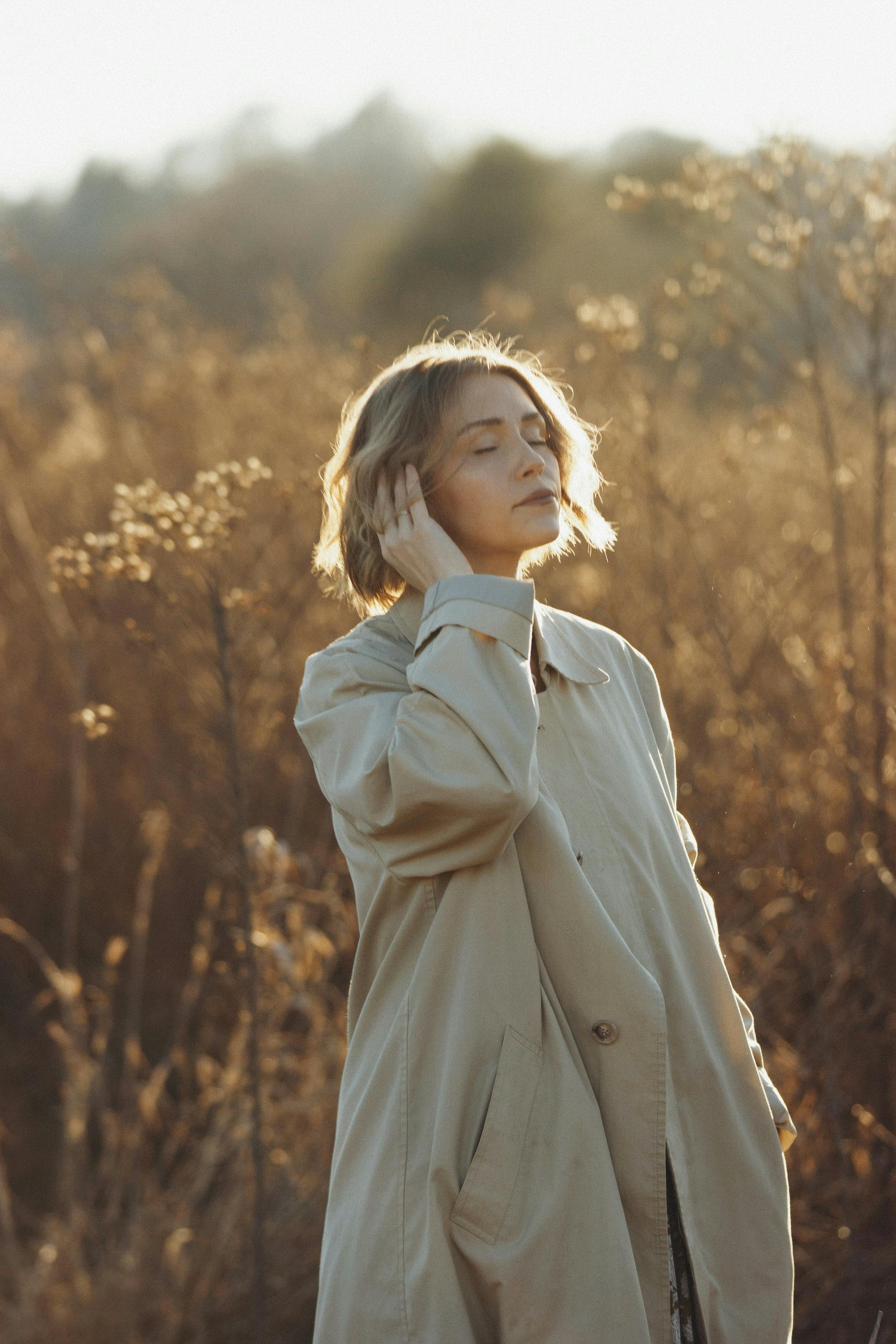 A woman in a trench coat enjoying a peaceful moment in a sunlit autumn field.