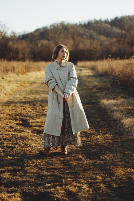 A serene portrait of a woman in a trench coat, standing in a sunlit autumn field, embodying peaceful elegance.