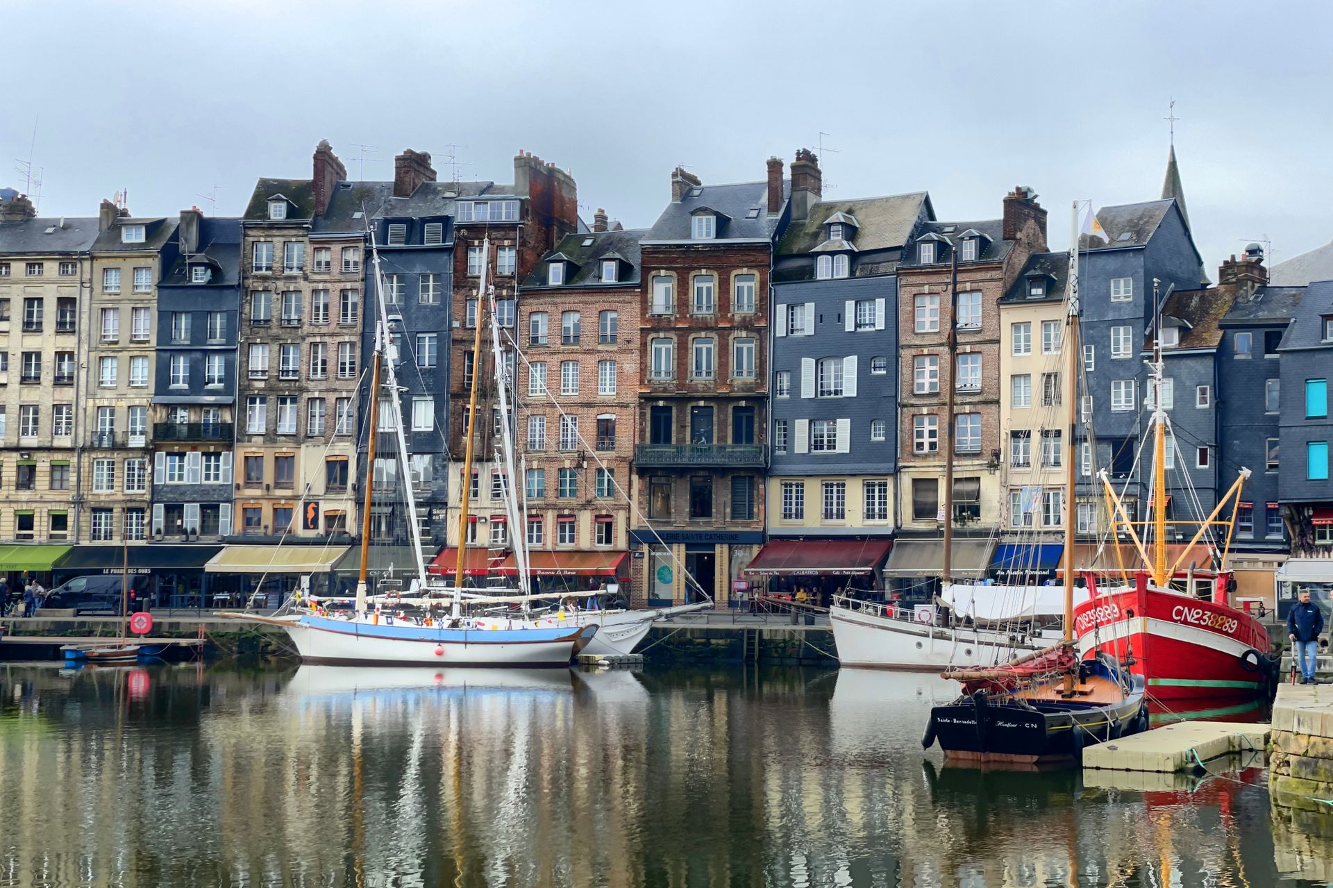 Picturesque view of Honfleur harbor with colorful historic buildings and sailboats reflecting in the calm water.