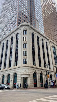 Elegant historic building surrounded by skyscrapers in a bustling city corner.