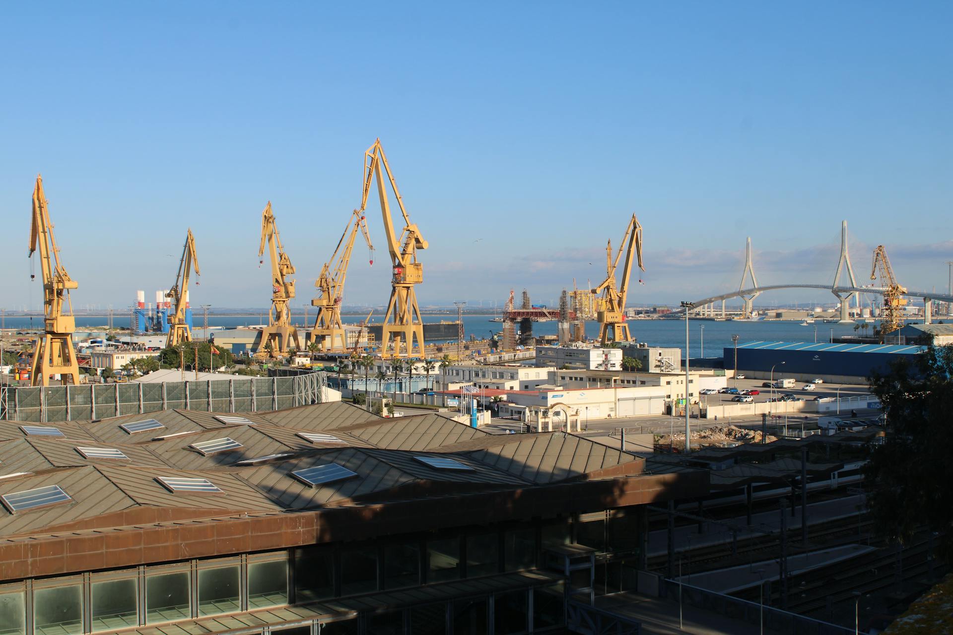 A panoramic view of Cádiz port with towering cranes and serene sea.
