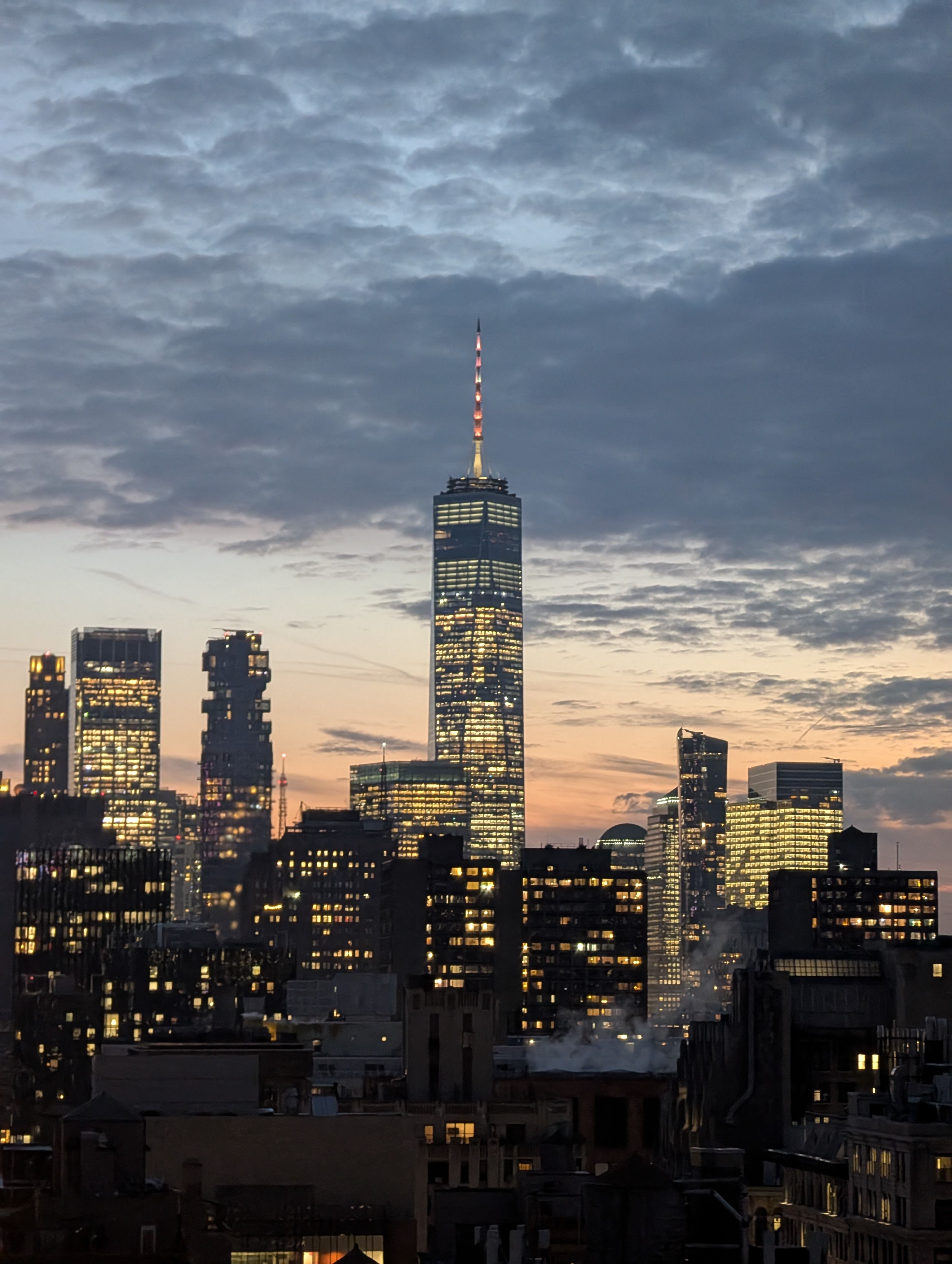 Stunning view of New York City skyline featuring the illuminated One World Trade Center at dusk.