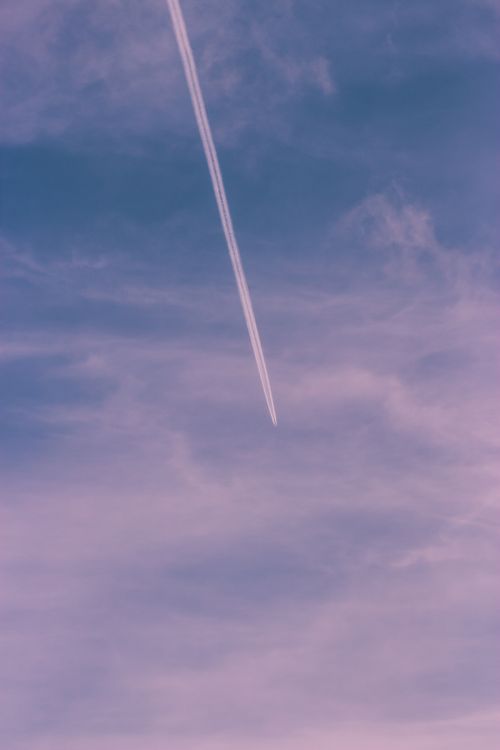 Free Airplane contrail streaks across a pastel-colored sky during sunset, creating a serene atmosphere. Stock Photo