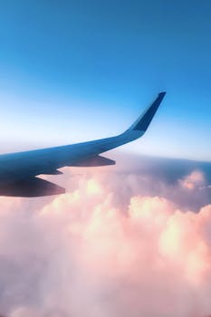 Scenic view from an airplane window showing the wing above pink clouds during sunrise.