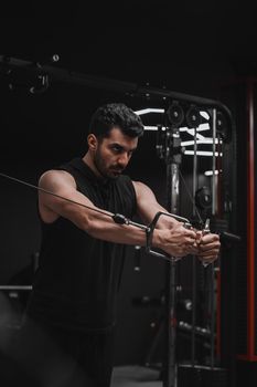 Male adult focused on strength training with a cable machine in the gym.