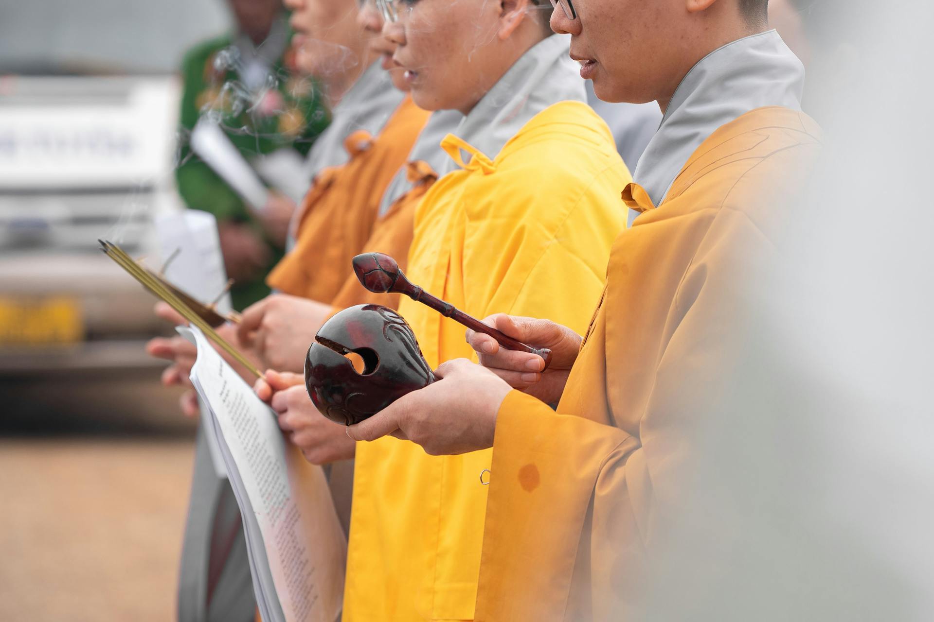 Buddhist monks in orange robes participate in a ceremonial practice, holding prayer tools and documents.