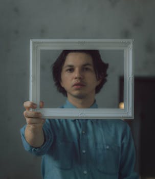 一名穿着牛仔衬衫的年轻人在室内拿着相框，创作了一幅独特的肖像