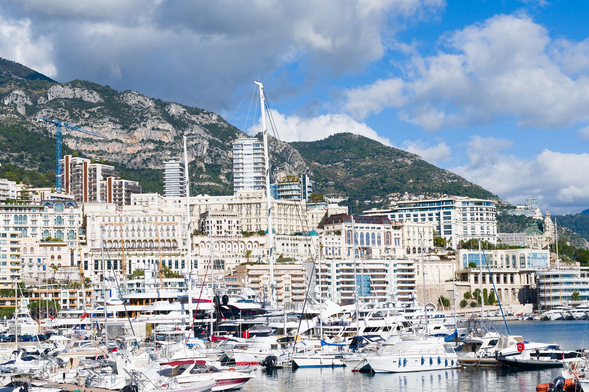 Stunning view of luxury yachts in Monaco harbor with city skyline and mountains in the background.