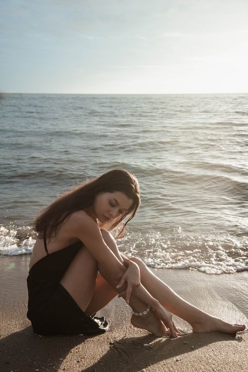 Free A serene portrait of a young woman sitting on a sandy beach with ocean waves in the background. Stock Photo