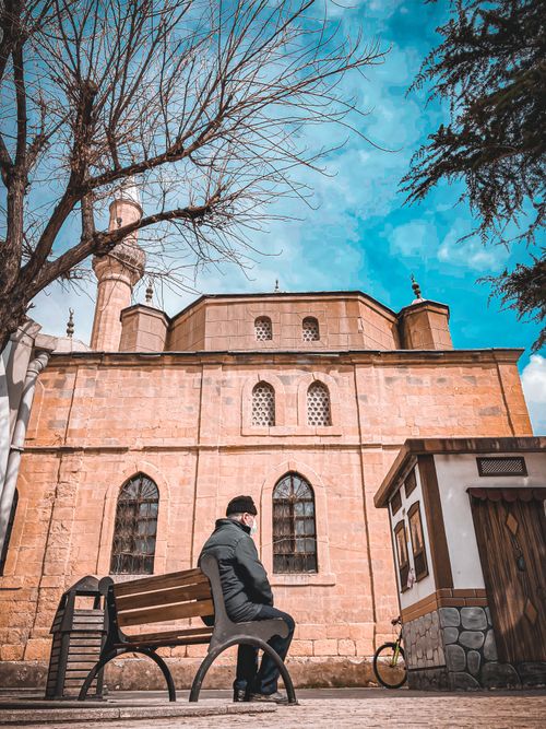 Free A person sits on a bench facing a historic mosque with a blue sky backdrop. Stock Photo