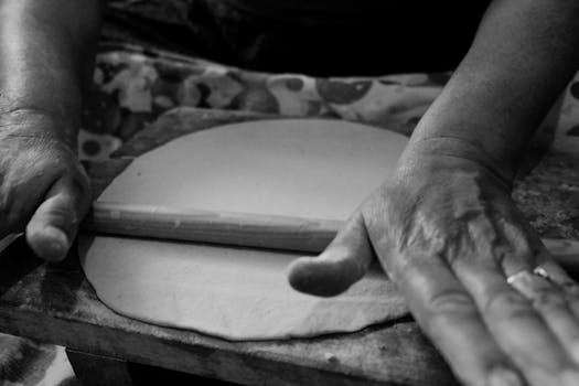 Monochrome close-up of hands rolling dough with a wooden pin.