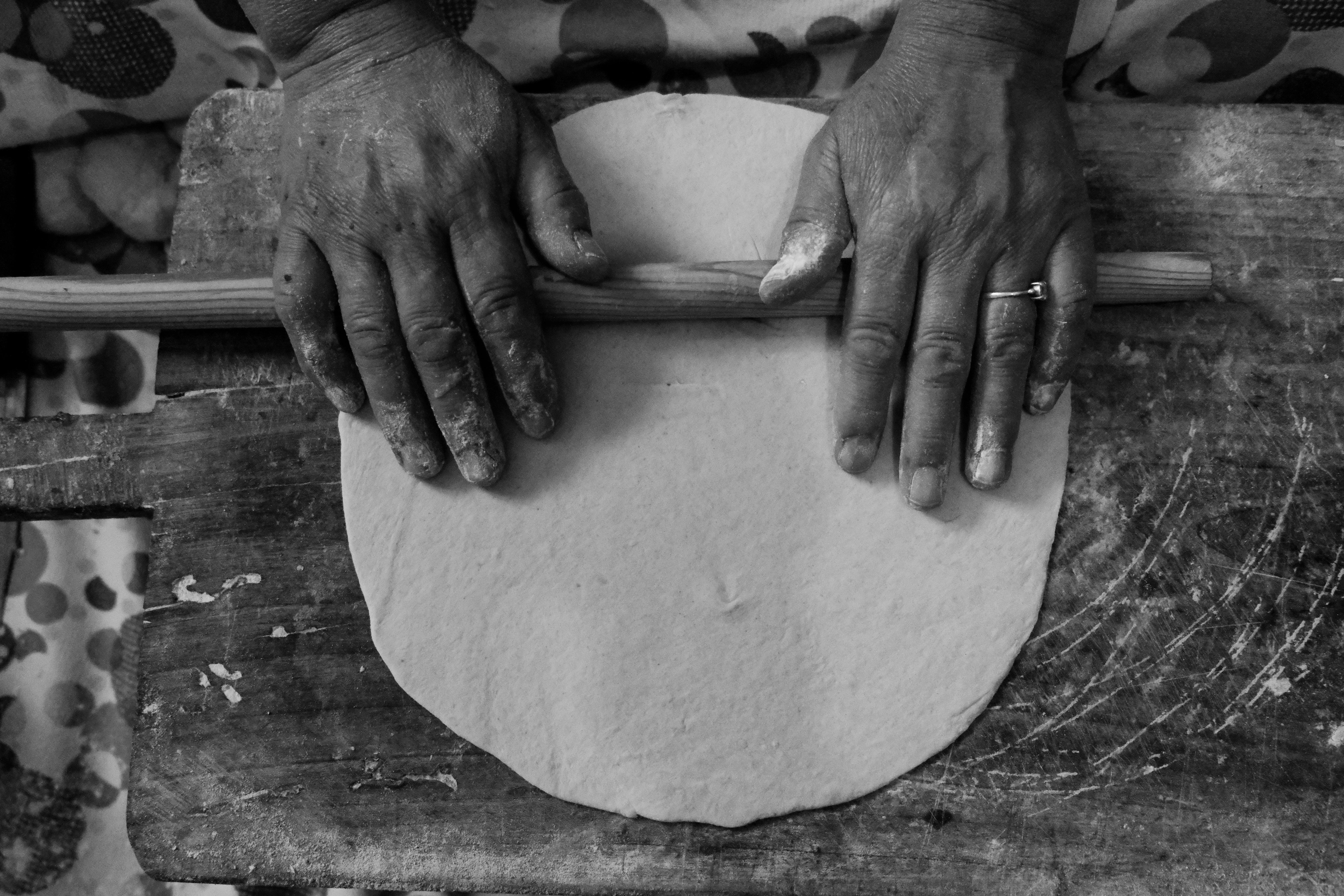 Hands rolling dough on a rustic wooden surface, creating homemade bread.