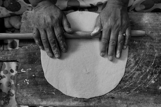 Hands rolling dough on a rustic wooden surface, creating homemade bread.