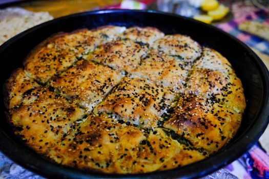 Golden brown savory pie with sesame seeds freshly baked in a black pan.
