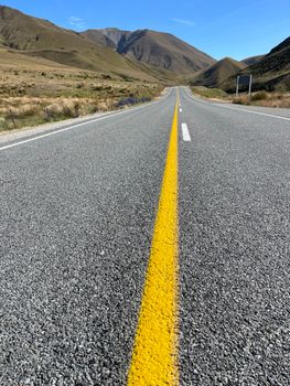 Open road with yellow line through mountains under a clear blue sky.
