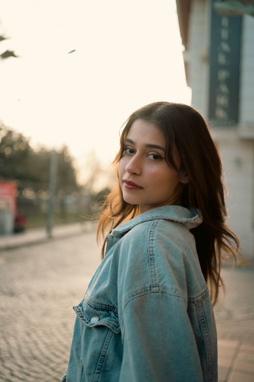 Free Portrait of a young woman wearing a denim jacket outdoors during a serene sunset. Stock Photo