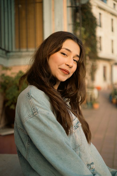 Free Portrait of a young woman in a denim jacket smiling in an urban setting during daylight. Stock Photo