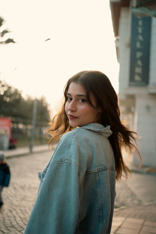 Free Portrait of a young woman in a denim jacket on a street at dusk, exuding a warm and soft mood. Stock Photo